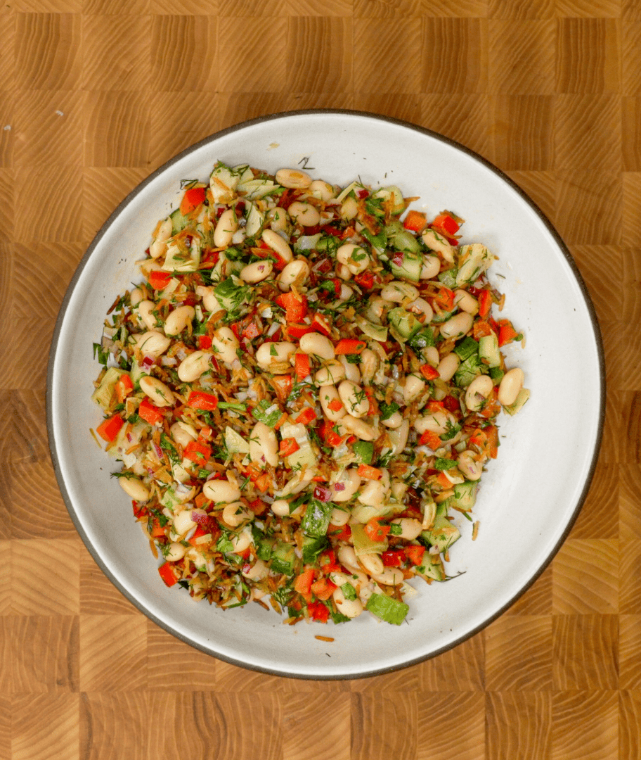 Overhead view of Calabrian Chili Crispy Rice and White Bean Salad in a white ceramic bowl, loaded with golden crispy Royal Basmati Rice tossed in Calabrian chili oil, cannellini beans, diced red bell pepper, cucumber, fresh dill, and herbs with a lemon Dijon dressing, on a wooden checkerboard surface