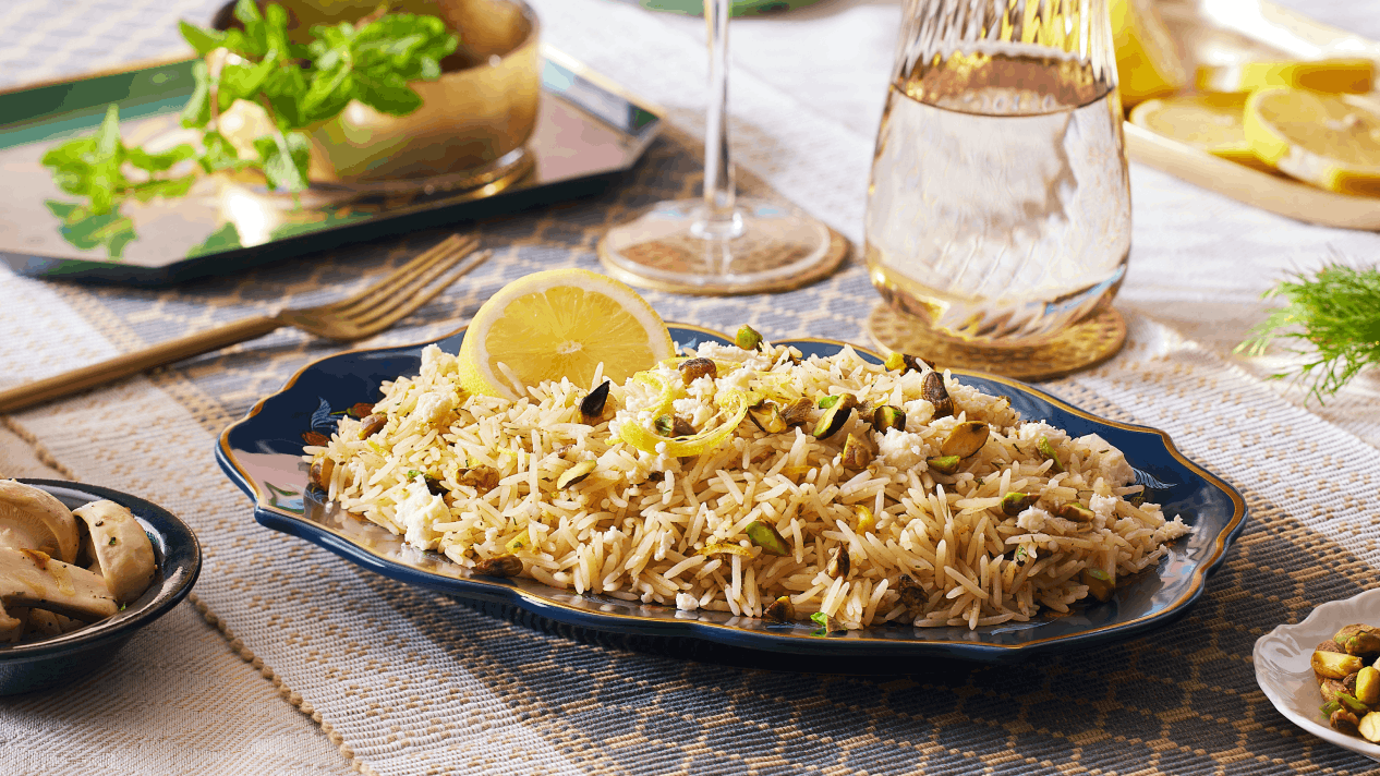 Mediterranean Lemon Herb Rice made with Royal® Chef's Secret™ Basmati Rice, topped with toasted pistachios and a lemon slice on an elegant navy blue plate, with fresh mint, dill, and lemon wedges in the background